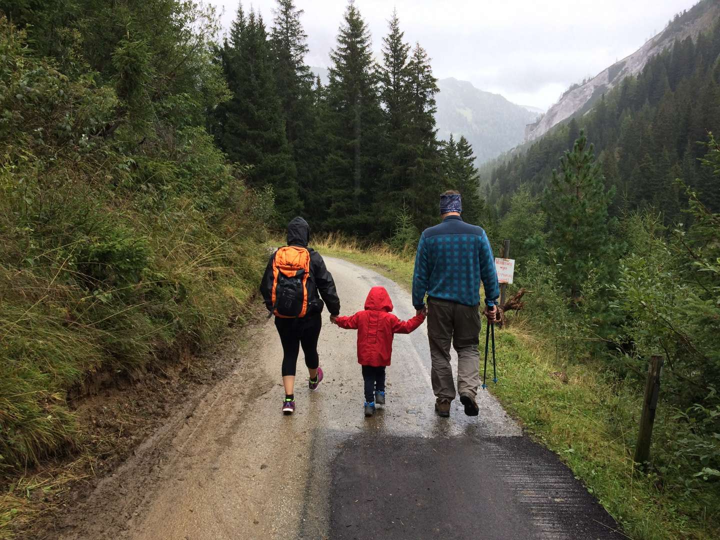 Mother, child and father hiking down a path on a rainy day